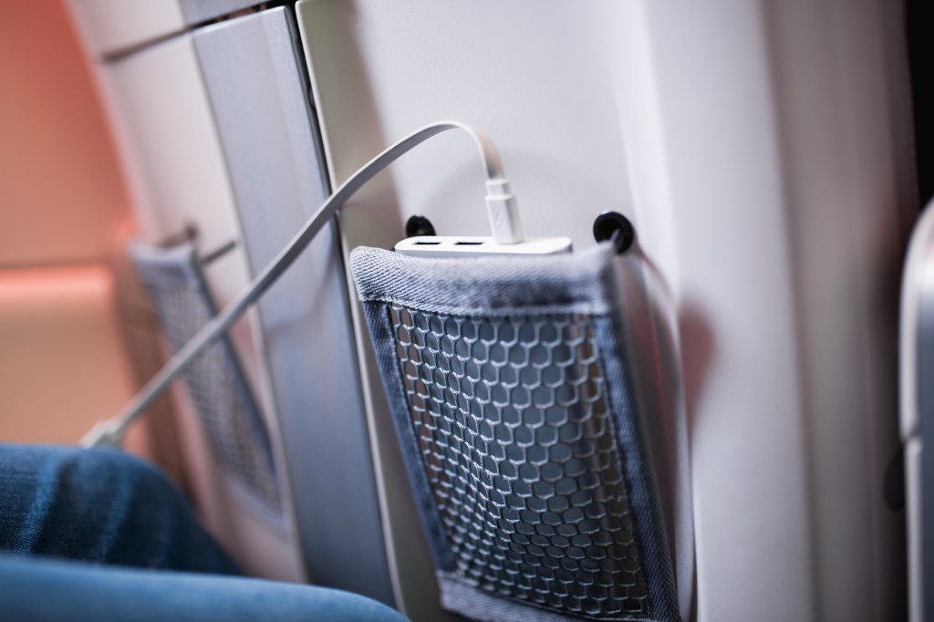 Portable charger and phone stored in airplane seat pocket for on-the-go recharging while traveling